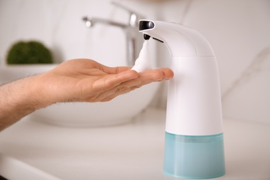 Photo of Man using automatic soap dispenser in bathroom, closeup