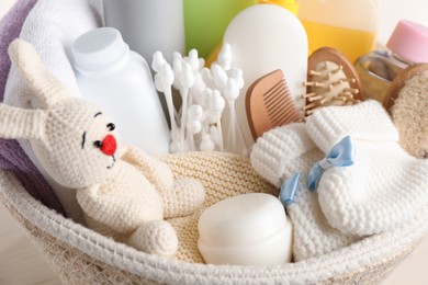 Photo of Wicker basket full of different baby cosmetic products, bathing accessories and toy on table, closeup