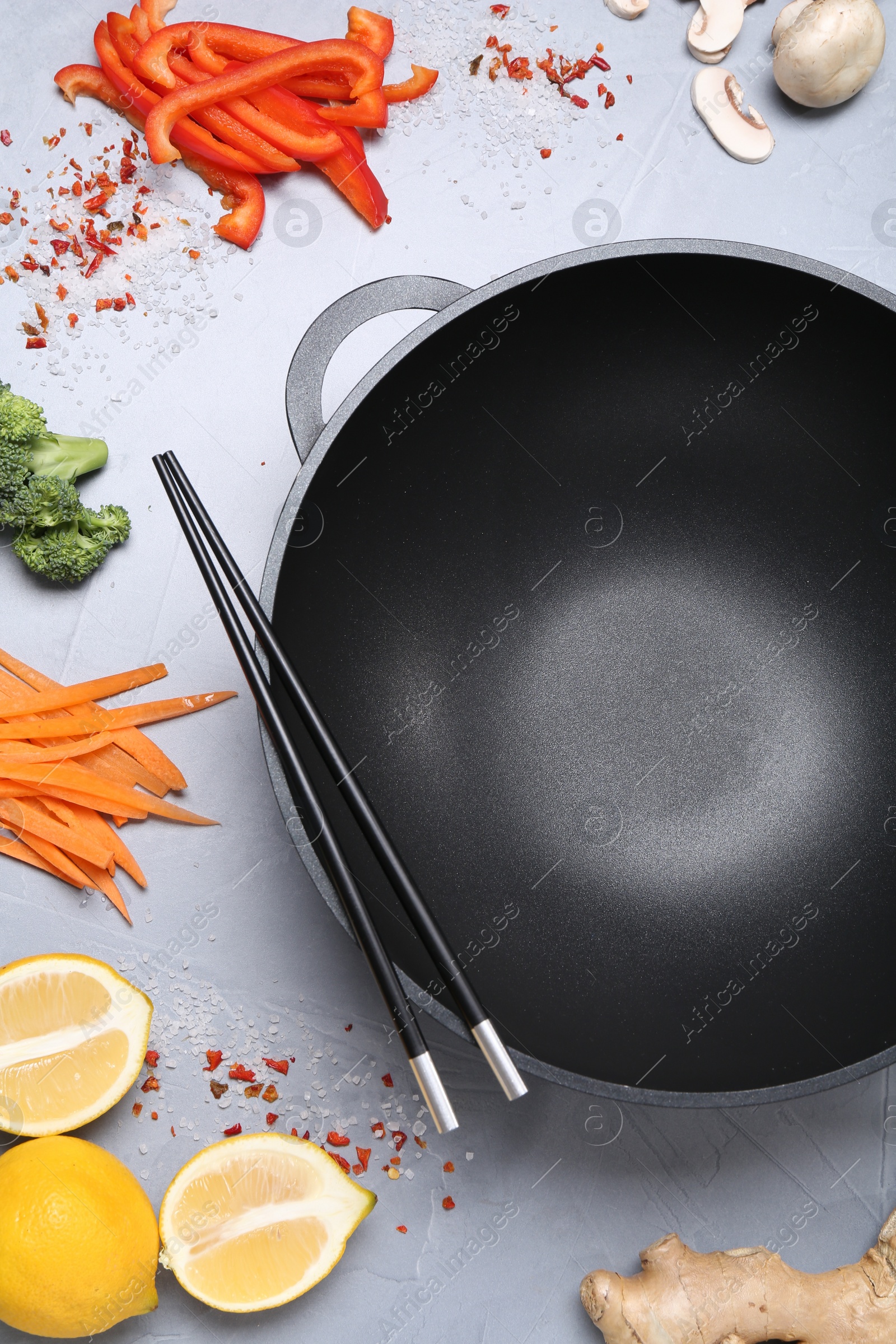 Photo of Wok, chopsticks and different products on grey table, flat lay