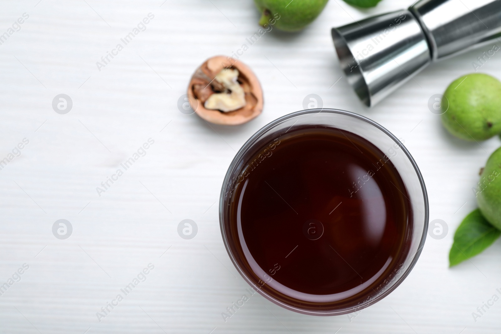 Photo of Delicious liqueur and fresh walnuts on white wooden table, flat lay. Space for text