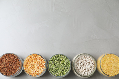 Glass jars with different types of groats on light grey table, flat lay. Space for text