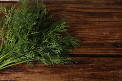 Photo of Sprigs of fresh green dill on wooden table, space for text