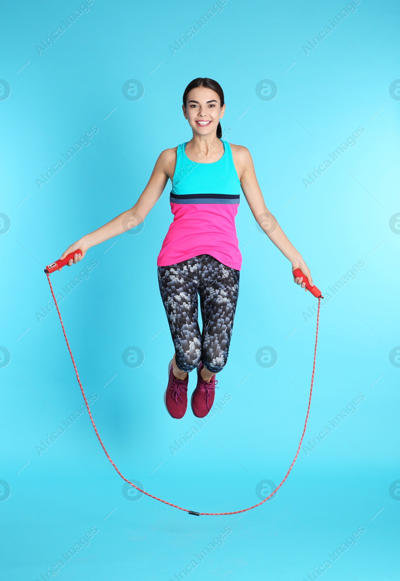 Photo of Full length portrait of young sportive woman training with jump rope on color background