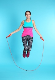 Full length portrait of young sportive woman training with jump rope on color background
