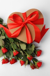Photo of Heart shaped gift box with bow and beautiful red roses on white background, flat lay