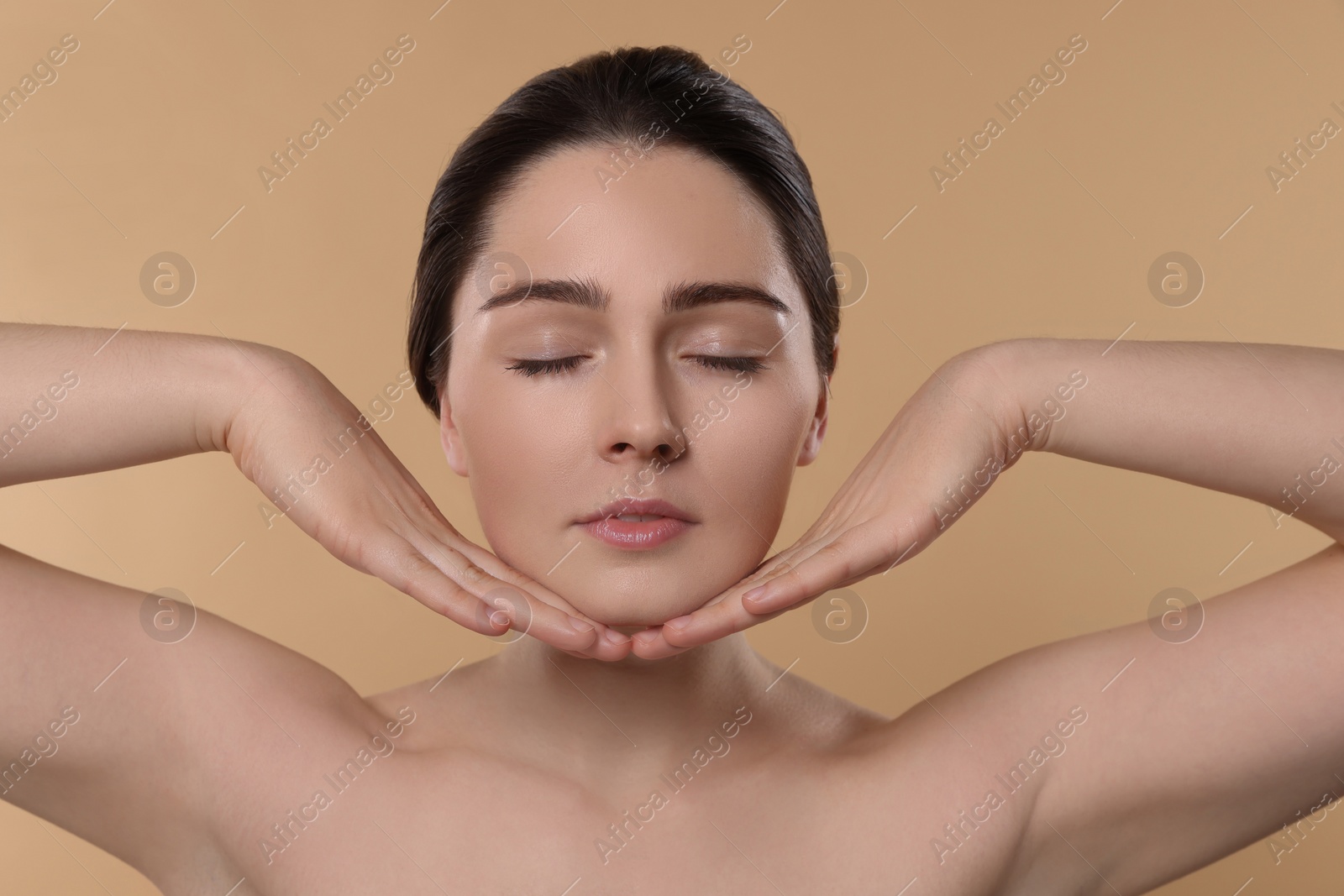 Photo of Young woman massaging her face on beige background