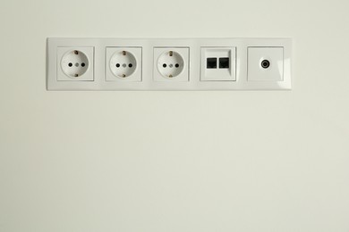 Many power sockets with ethernet and TV coax plates on white wall indoors. Space for text