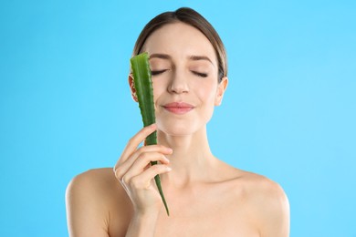 Young woman with aloe leaf on light blue background