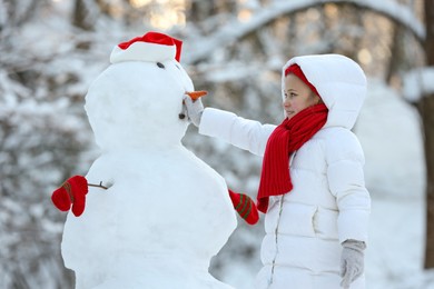 Photo of Cute little girl making snowman in winter park