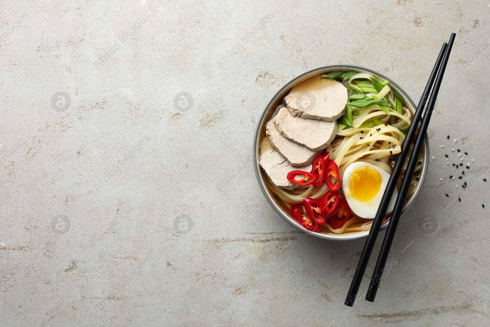 Photo of Delicious ramen in bowl and chopsticks on light textured table, top view. Noodle soup