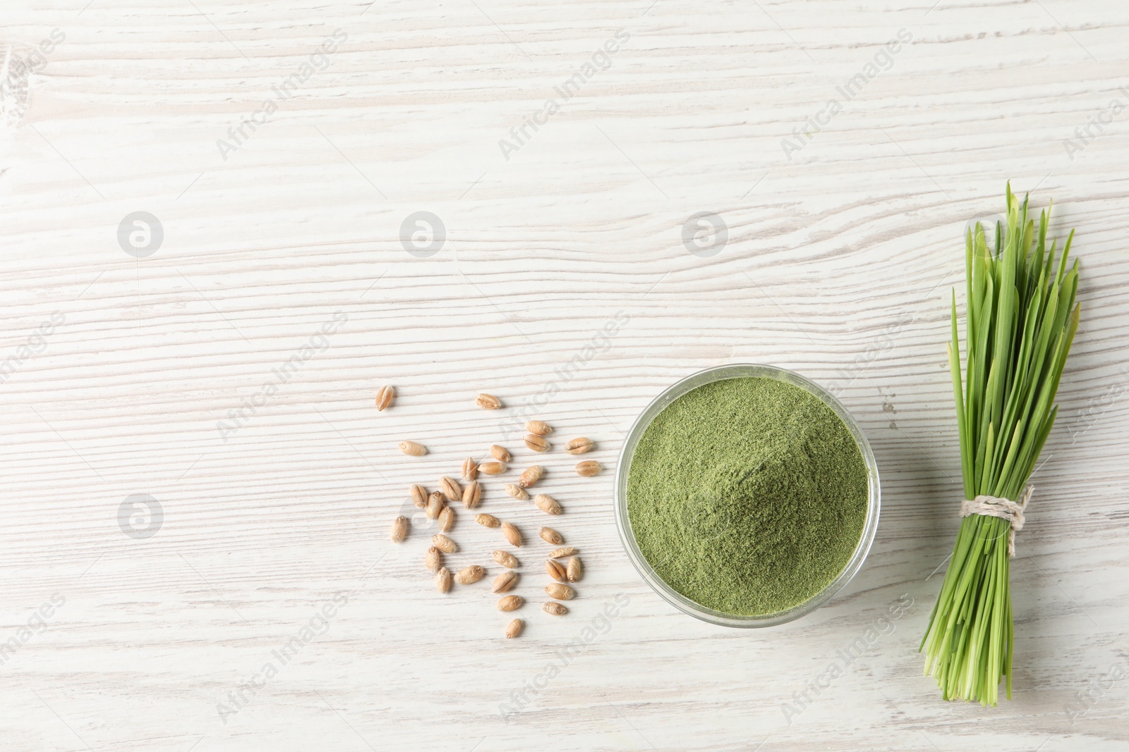 Photo of Wheat grass powder in bowl, seeds and fresh sprouts on white wooden table, flat lay. Space for text