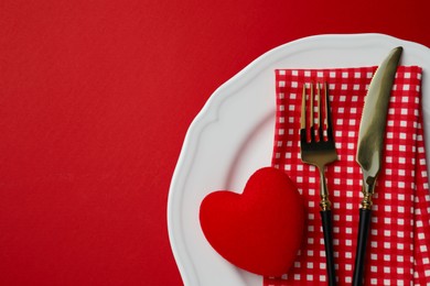 Photo of Plate with cutlery and decorative heart on red table for romantic dinner, top view. Space for text