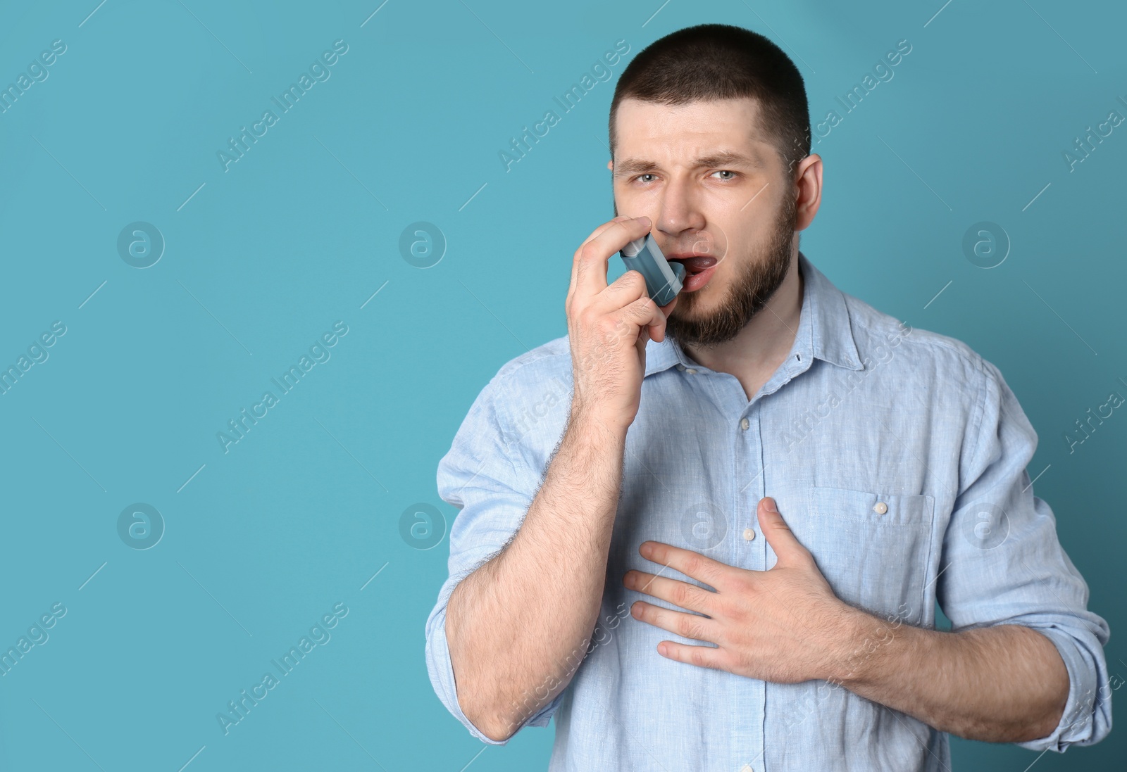 Photo of Young man using asthma inhaler on color background with space for text