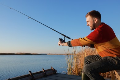 Fisherman with fishing rod at riverside on sunny day