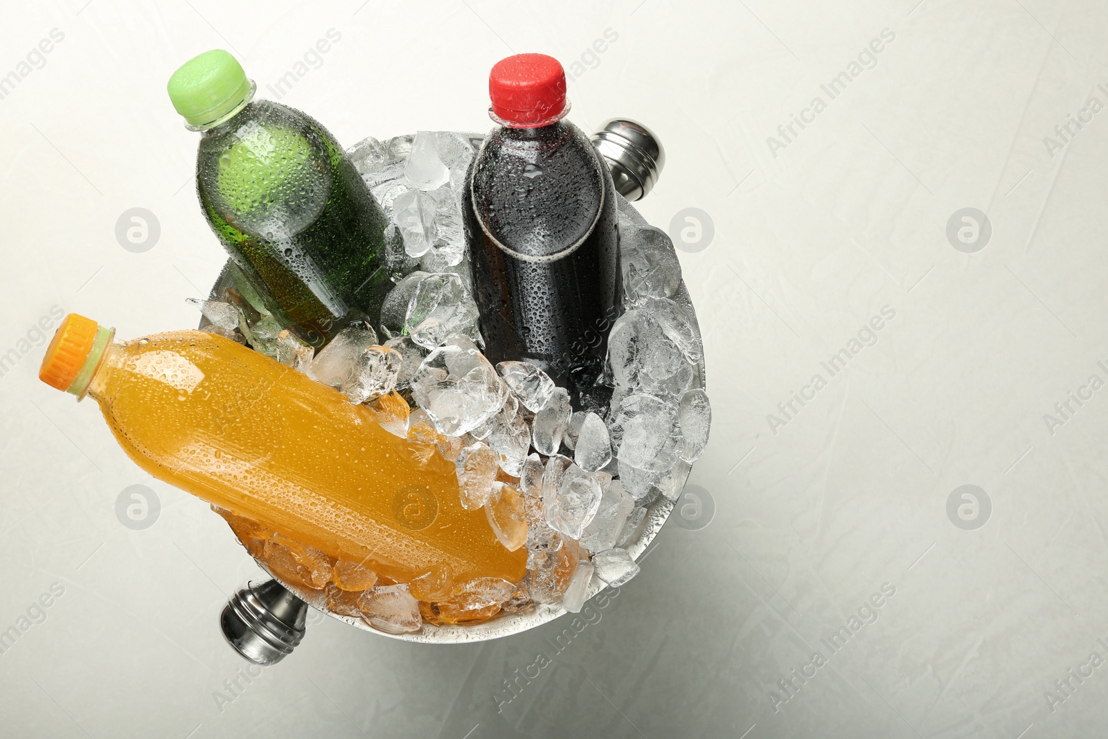Photo of Different soda drinks in metal bucket with ice on light grey table, top view