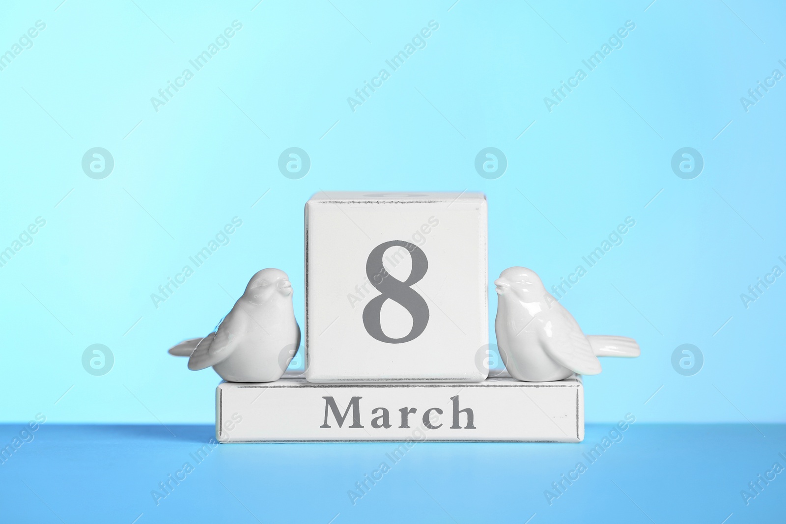 Photo of Wooden calendar and decorative birds on table against color background. International Women's Day