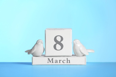 Wooden calendar and decorative birds on table against color background. International Women's Day