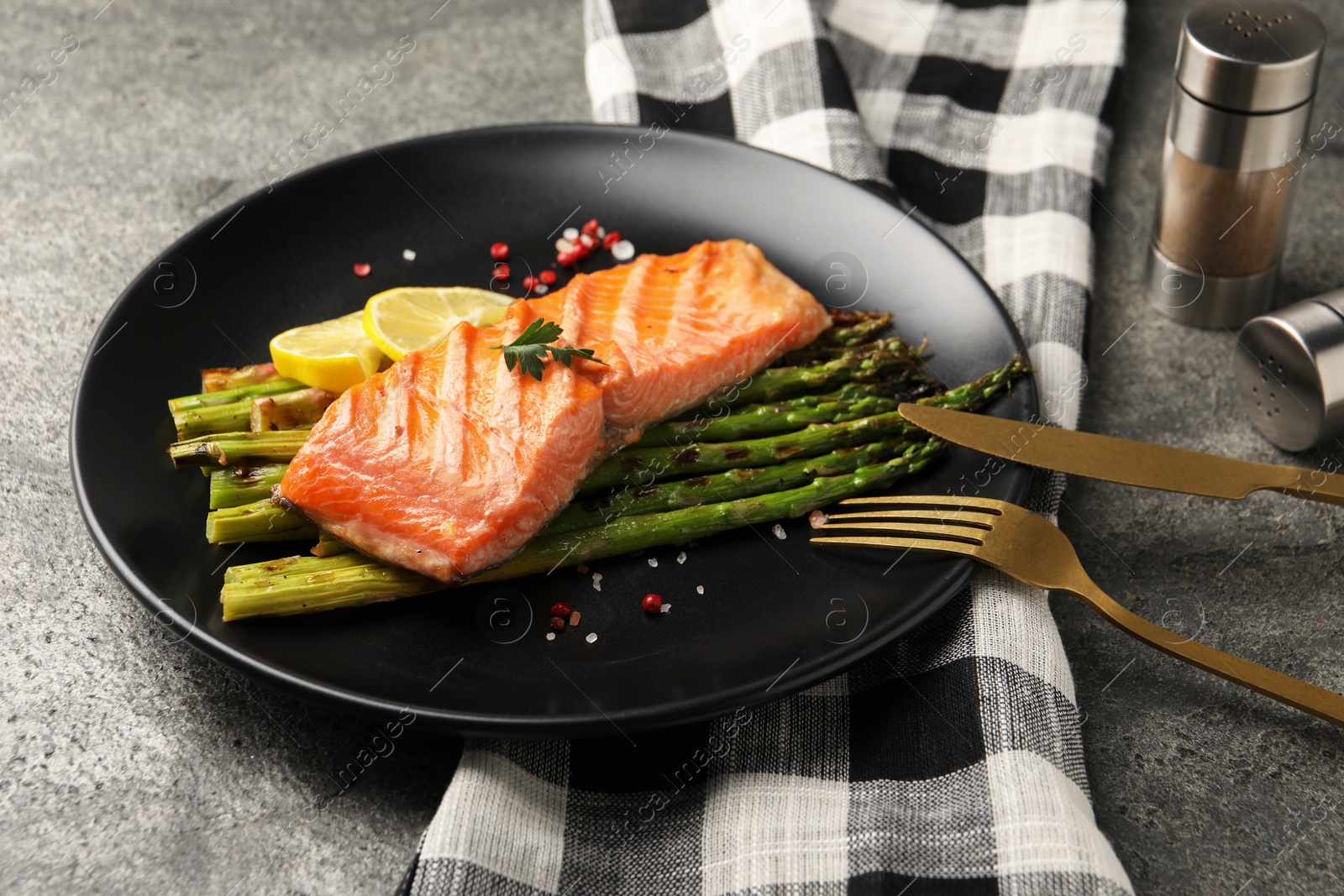 Photo of Tasty grilled salmon with asparagus, lemon and spices served on grey table, closeup