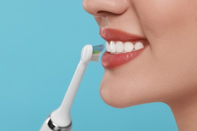 Photo of Woman brushing her teeth with electric toothbrush on light blue background, closeup. Space for text