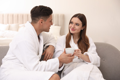 Photo of Happy couple in bathrobes with coffee on sofa at home