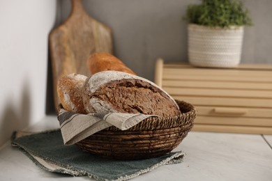 Photo of Wicker bread basket with freshly baked loaves on white marble table in kitchen