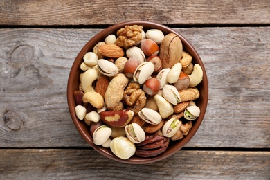 Bowl with mixed organic nuts on wooden background, top view