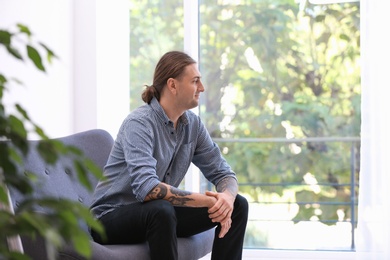 Photo of Young man with stylish tattoos at home. Space for text