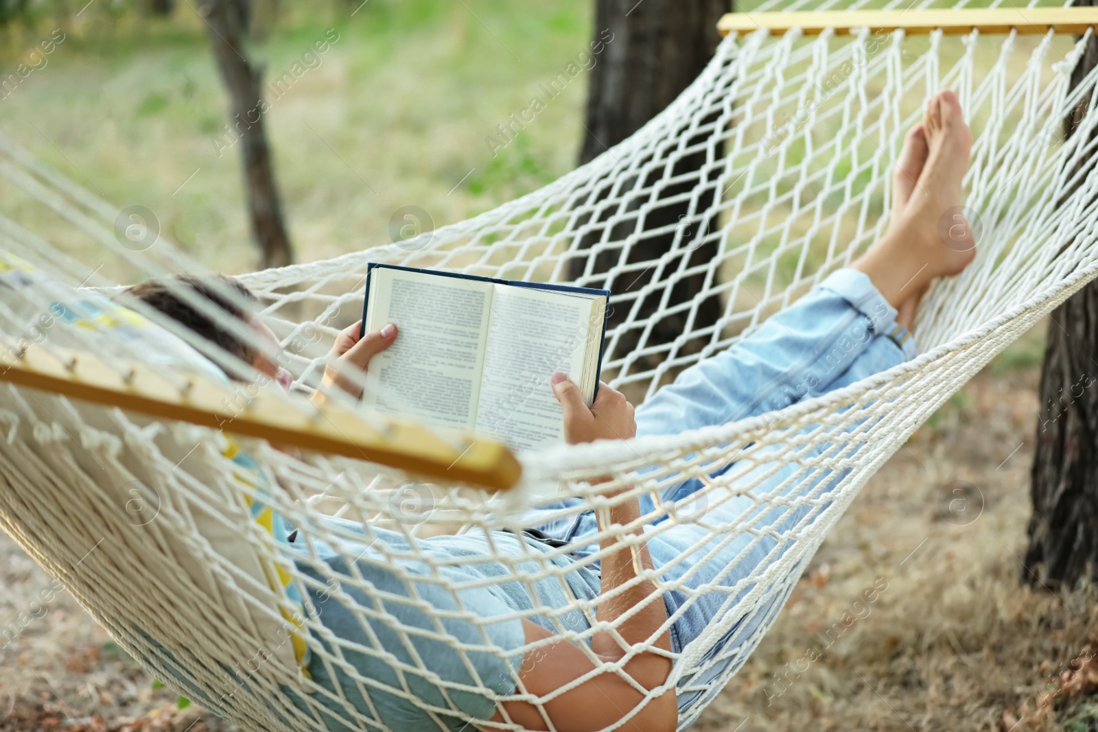 Photo of Man reading book in comfortable hammock at green garden