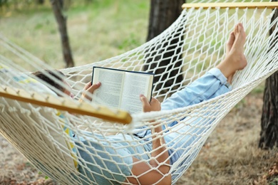 Man reading book in comfortable hammock at green garden