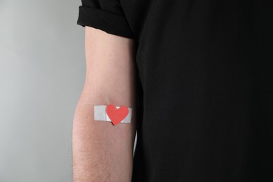 Blood donation concept. Man with adhesive plaster on arm against grey background, closeup