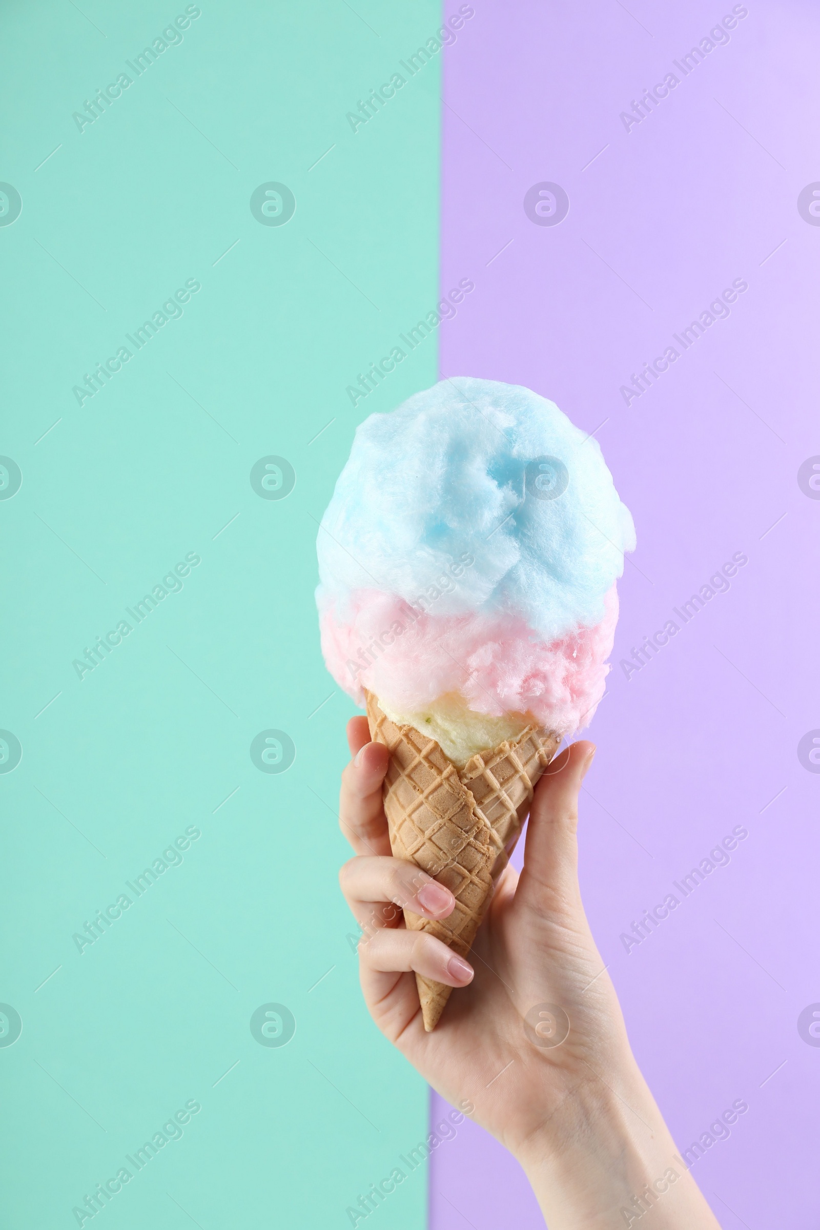 Photo of Woman holding waffle cone with cotton candy on color background, closeup