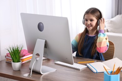 Photo of E-learning. Cute girl using computer and headphones during online lesson at table indoors