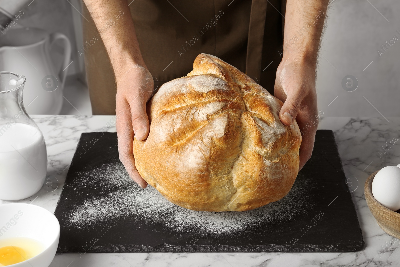 Photo of Male baker holding loaf of bread over kitchen table, closeup