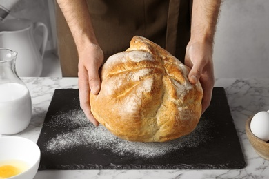 Photo of Male baker holding loaf of bread over kitchen table, closeup