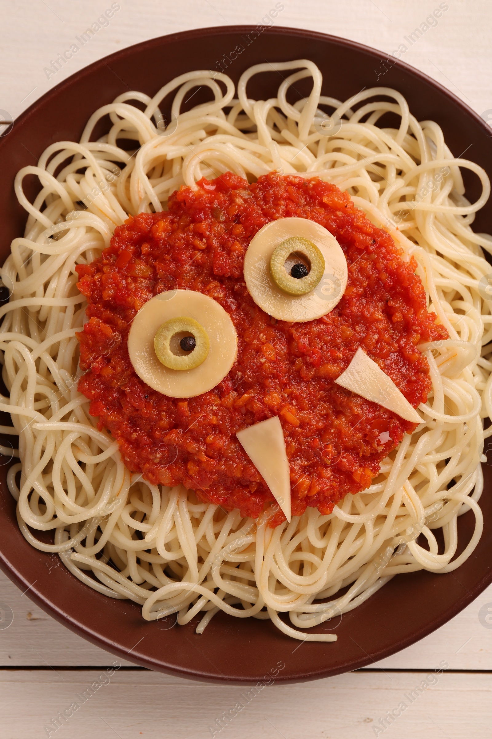 Photo of Plate with funny monster made of tasty pasta on white wooden table, top view. Halloween food