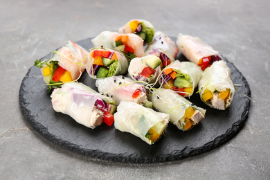 Photo of Delicious rolls wrapped in rice paper on grey table