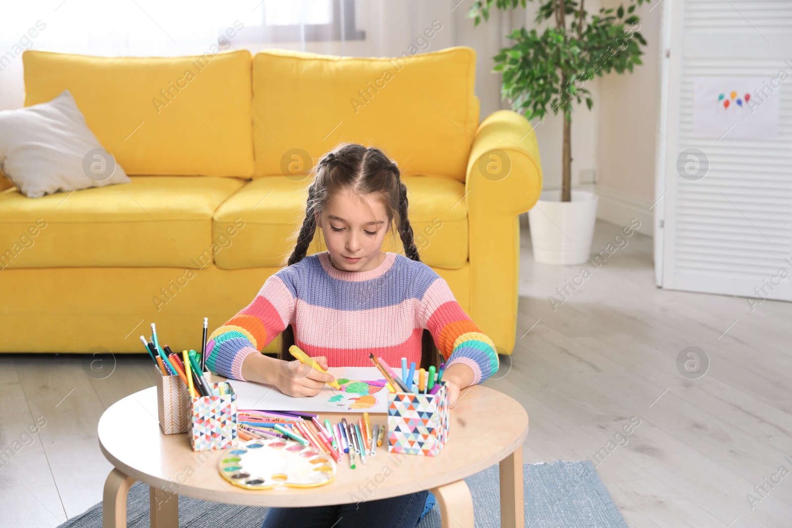 Photo of Little girl drawing picture at table with painting tools indoors
