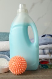 Photo of Orange dryer ball, detergents, clean towels and clothes on wooden table