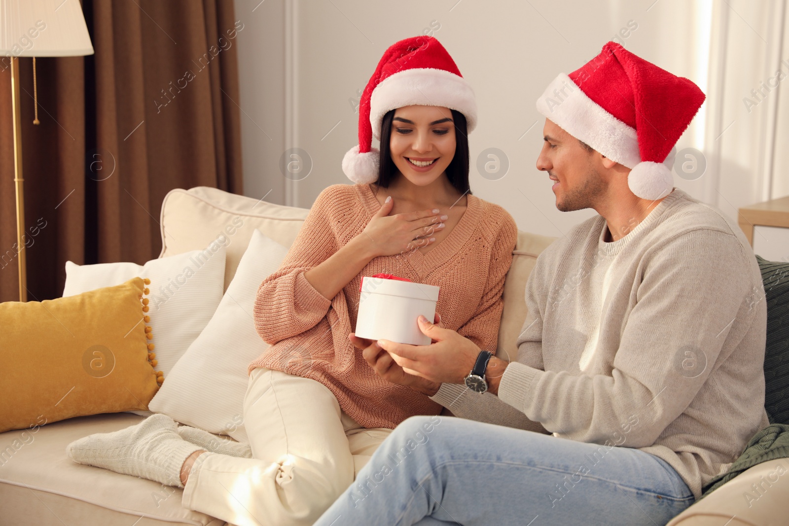 Photo of Happy young couple with Christmas gift sitting on sofa in living room