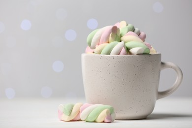 Ceramic cup with colorful marshmallows on white table against blurred lights