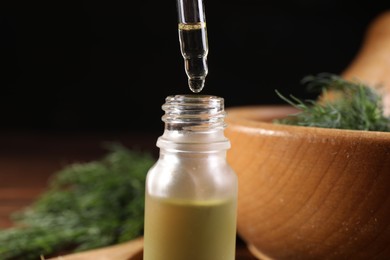 Photo of Dripping dill essential oil from pipette into bottle against black background, closeup