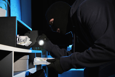 Photo of Thief taking money out of steel safe indoors at night