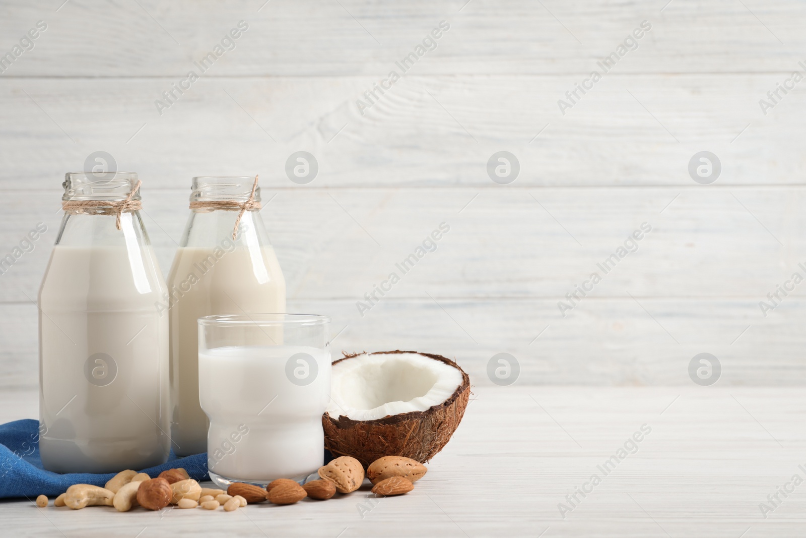 Photo of Different nut milks on white wooden table. Space for text