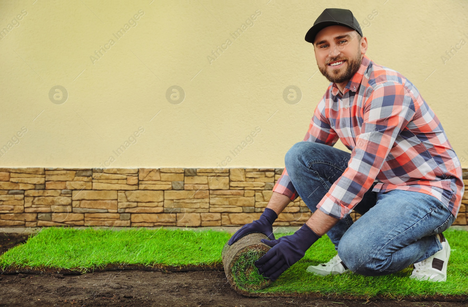 Photo of Young man laying grass sod on ground at backyard, space for text