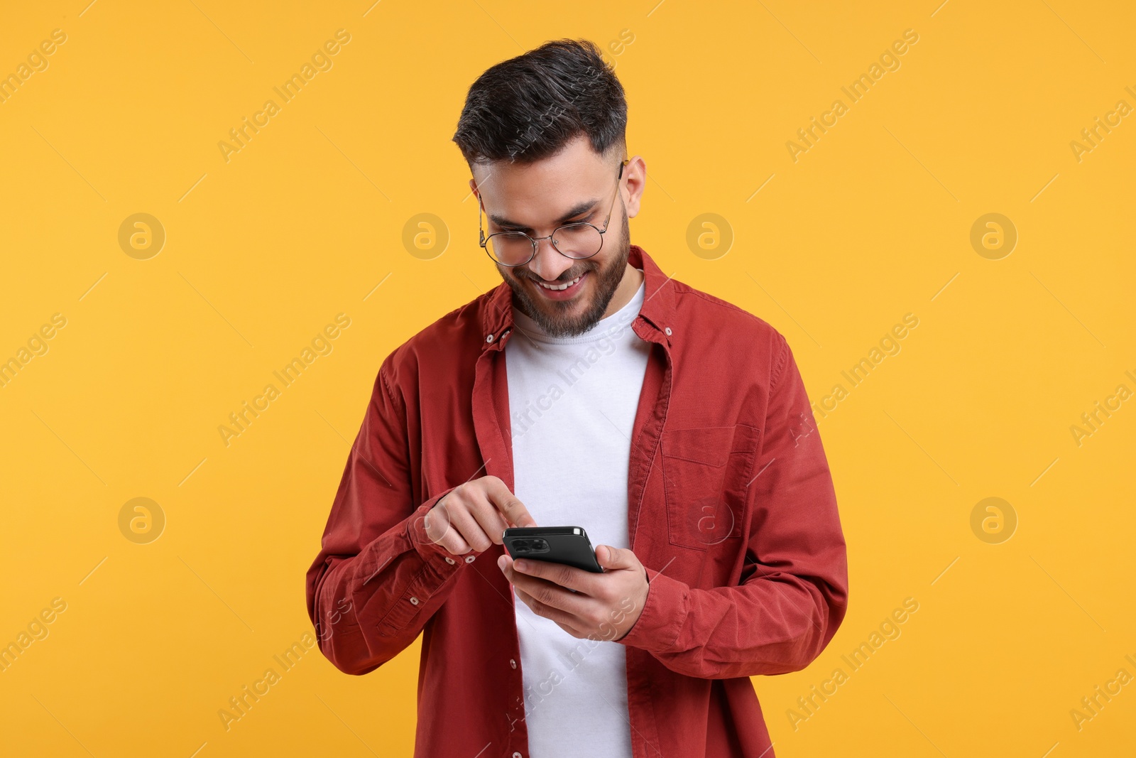 Photo of Happy young man using smartphone on yellow background