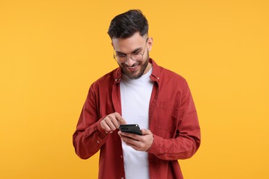 Happy young man using smartphone on yellow background