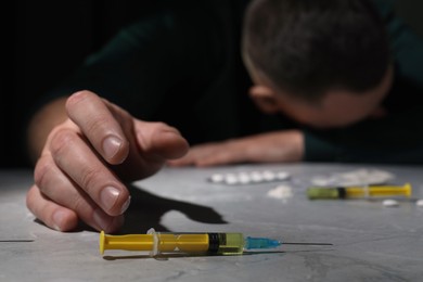 Overdosed man at grey table, focus on syringe with drugs