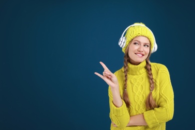 Young woman listening to music with headphones on dark blue background, space for text