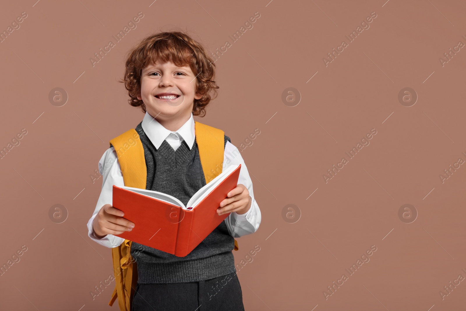 Photo of Happy schoolboy with backpack and book on brown background