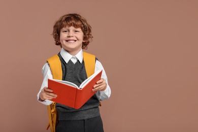 Happy schoolboy with backpack and book on brown background